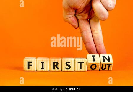Premier dans premier sorti.L'homme d'affaires tourne des cubes en bois et change de mots d'abord en premier.Belle table orange, fond orange.Entreprise Banque D'Images