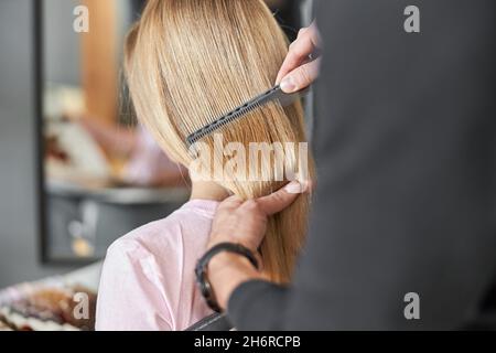 Le coiffeur de Pofessionnal est peignant les cheveux d'une belle femme blonde caucasienne dans le salon moderne Banque D'Images