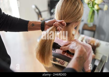 Le coiffeur de Pofessionnal est peignant les cheveux d'une belle femme blonde caucasienne dans le salon moderne Banque D'Images