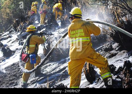 Les pompiers de la ville de San Diego travaillent un feu de broussailles près de la route d'état 52, appliquant de la mousse de lutte contre le feu à la dense sous-croissance. Banque D'Images