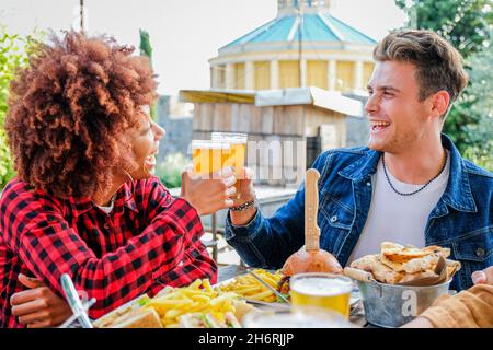 Groupe d'amis heureux multiethniques vivant un style de vie sain et relaxant tout en buvant de la bière au restaurant de pub extérieur - les jeunes appréciant des boissons Banque D'Images