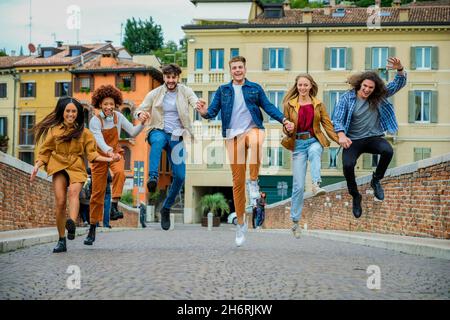 Groupe multiethnique de jeunes fous ayant plaisir à marcher et à sauter dans la rue de la ville - concept de style de vie et d'amitié Banque D'Images