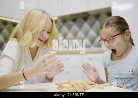 Deux filles ont plaisir à jouer Jenga ensemble - jeu de société pour enlever des blocs de bois et le concept de loisirs pour les enfants. Banque D'Images