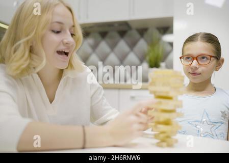 Deux filles ont plaisir à jouer Jenga ensemble - jeu de société pour enlever des blocs de bois et le concept de loisirs pour les enfants. Banque D'Images