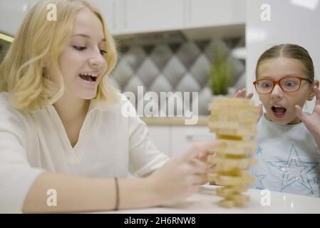 Deux filles ont plaisir à jouer Jenga ensemble - jeu de société pour enlever des blocs de bois et le concept de loisirs pour les enfants. Banque D'Images