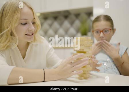 Deux filles ont plaisir à jouer Jenga ensemble - jeu de société pour enlever des blocs de bois et le concept de loisirs pour les enfants. Banque D'Images