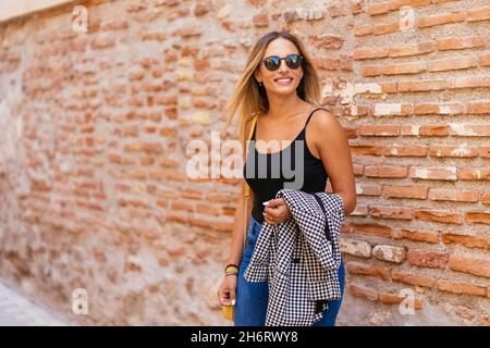 Femme élégante debout près du mur de briques en ville Banque D'Images