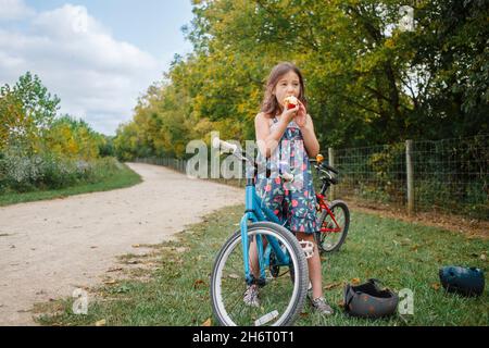 Une petite fille à vélo prend une pause pour manger de la pomme en été Banque D'Images