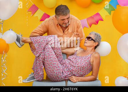 Couple âgé sur fond jaune.La femme repose sur les chaises et l'homme atteint pour elle Banque D'Images