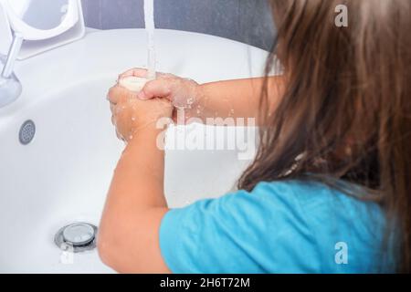 L'enfant lave ses mains avec du savon sous l'eau courante dans la salle de bains Banque D'Images