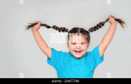 Un enfant heureux tenant des queues de porc et riant sur fond gris Banque D'Images