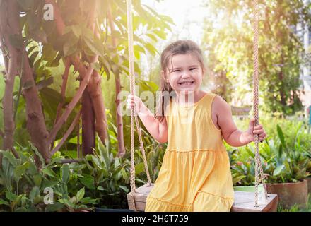 Portrait d'un enfant sur une balançoire.Une fille dans une robe jaune passe du temps dans l'arrière-cour Banque D'Images