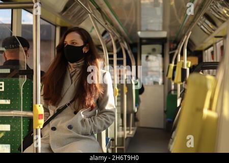 Les personnes de race blanche de plusieurs âges dans le visage masques de protection conduire dans un bus.Jeune femme du millénaire regardant la fenêtre dans les transports publics. Banque D'Images