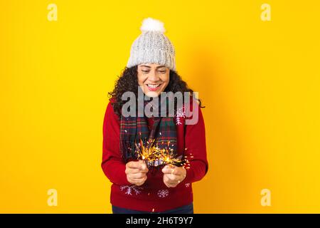 Femme hispanique adulte tenant des lumières pétillantes de noël pour la posada mexicaine à noël sur fond jaune au Mexique Amérique latine Banque D'Images