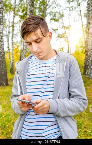 Jeune homme tient un téléphone mobile dans la forêt d'automne Banque D'Images