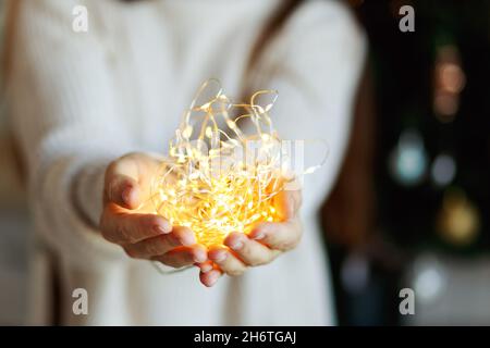 Miracle de Noël - une femme en chandail blanc tient la guirlande lumineuse de lumière LED dans les mains, arrière-plan bokeh. Banque D'Images