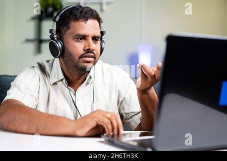 FAT man parle en toute confiance lors d'un appel vidéo sur un ordinateur portable équipé d'un micro-casque tout en travaillant au bureau à domicile en raison du concept de visioconférence Covid-19 Pandemic Banque D'Images