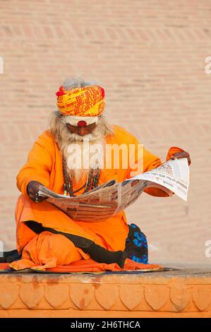 INDE, UTTAR PRADESH, VARANASI, SADHU LISANT UN JOURNAL SUR LES RIVES DU GANGE Banque D'Images