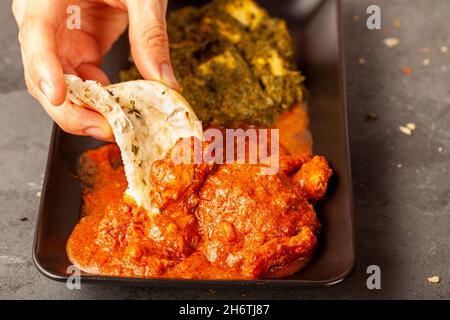 Une femme mange une délicieuse cuisine indienne avec divers plats.Elle plonge le pain naan dans le curry.Concept pour les variétés de cuisine asiatique.Tikka masala et Banque D'Images