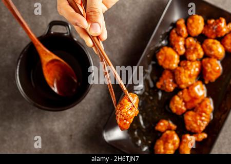 Une personne mange un délicieux poulet mandarin orange, un plat chinois américain à l'aide de baguettes en bois.La sauce est servie dans un bol en porcelaine.Bac foncé Banque D'Images