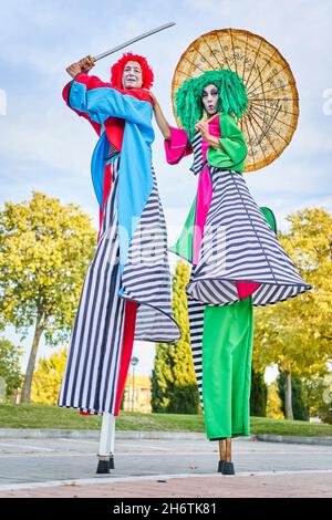 Une multitude d'artistes talentueux et créatifs avec un art du visage en costumes colorés et des perruques debout sur des pilotis dans le parc, avec un parapluie asiatique et une épée pendant le spectacle, le jour du soleil Banque D'Images