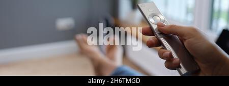 Une femme est assise sur un canapé et tient la télécommande du téléviseur dans ses mains Banque D'Images