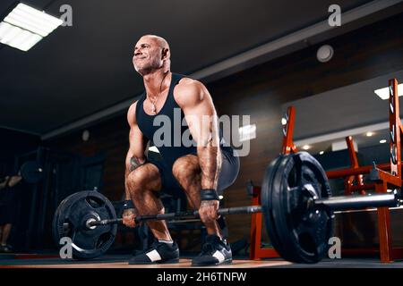 Sportif bald adulte poids de levage exercice dans la salle de gym faire de l'exercice pour les muscles du dos avec barbell Banque D'Images