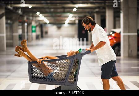 Un couple adulte s'amuse au garage du supermarché avec un chariot à roulettes.Les gens et la famille dans les activités de shopping jouent et en Banque D'Images