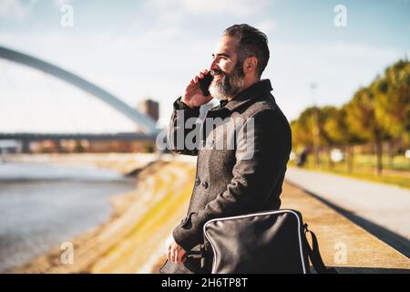 Homme d'affaires est assis à l'extérieur de la ville et parle au téléphone Banque D'Images