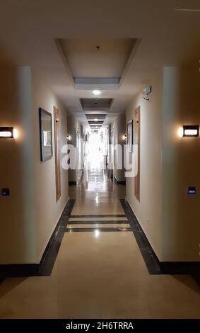 Long couloir menant à la perspective, une rangée de pièces sur les côtés, lumière vive à la fin tout est éclairé par des lampes Banque D'Images