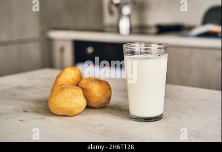 Un verre transparent avec du lait de pomme de terre sur la table à côté des tubercules de pomme de terre. Banque D'Images