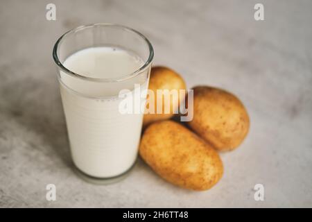 Un verre transparent avec du lait de pomme de terre sur la table à côté des tubercules de pomme de terre. Banque D'Images