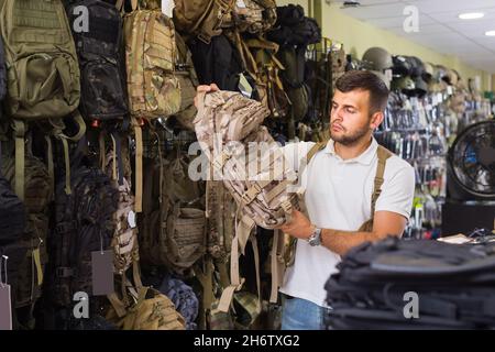 Homme choisissant un pistolet à sac à dos en textile dans un magasin militaire Banque D'Images