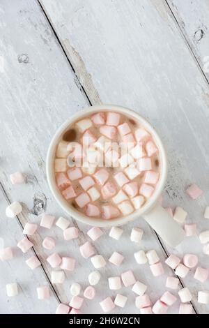 Vue de dessus d'une tasse remplie de chocolat chaud et de mini guimauves sur bois blanc altéré avec espace de copie. Banque D'Images