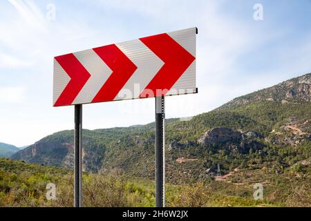 Panneau de direction de virage dangereux.Panneau de direction de virage dangereux placé sur le bord de la route en terrain montagneux. Banque D'Images