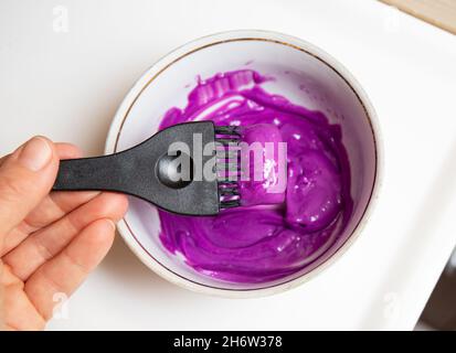 Bol en céramique avec un mélange de colorant pastel violet pour les cheveux, à l'intérieur est un pinceau à colorant, un pinceau à colorier pour les cheveux. Banque D'Images