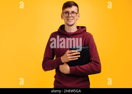 L'homme chrétien avec des lunettes tient une Bible dans ses mains.Lecture de la Bible sur fond jaune isolé.Concept de foi, de spiritualité et de religion.La paix, Banque D'Images