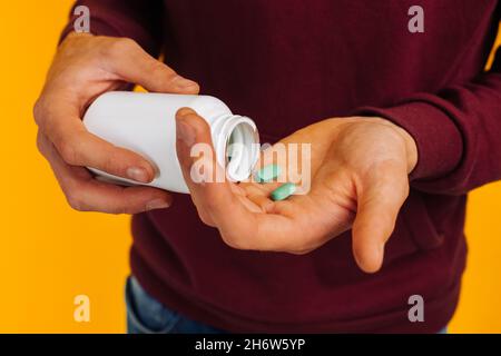 Main de gros plan tient des pilules, l'homme verse des pilules de la bouteille pour prendre des médicaments sur fond jaune.Soins de santé, traitement, suppléments concept photo Banque D'Images