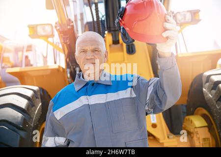 Le conducteur de pelle hydraulique en casque de chantier se tient à l'équipement de construction, concept de portrait d'homme industriel. Banque D'Images