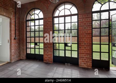 Wratting, Angleterre - août 19 2019 : fenêtre en orangerie voûtée et portes dans une maison britannique traditionnelle avec sol carrelé et vue sur les jardins au-delà. Banque D'Images