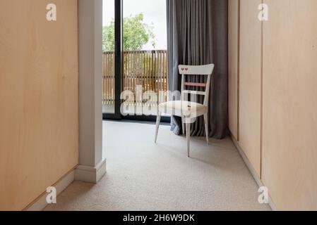 Dry Drayton, Angleterre - 2 août 2019 : chaise à vélo solitaire dans le coin d'une pièce à côté d'une grande porte coulissante vitrée qui s'ouvre sur un balcon Banque D'Images