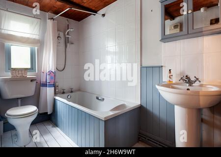 Kedington, Suffolk - novembre 19 2019: Petite salle de bains et wc à l'intérieur du cottage britannique avec murs carrelés et lambrissés, lavabo, toilettes et baignoire Banque D'Images