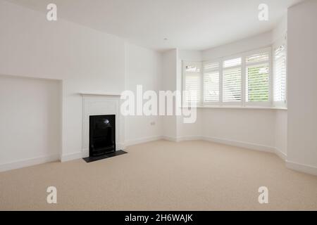 Cambridge, Angleterre - juillet 31 2019: Chambre vide dans la maison rénovée avec cheminée et baie vitrée avec stores peints en blanc Banque D'Images
