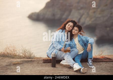 Une jeune mère et son fils adolescent en denim assis sur une couverture et boire du thé chaud d'un thermos Banque D'Images