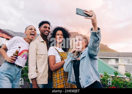 Des amis heureux prenant un selfie de groupe en plein air.Quatre amis posant pour un selfie tout en faisant la fête sur le toit.Groupe d'amis multiculturels Banque D'Images