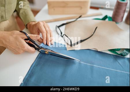 La couturière avec ciseaux coupe le tissu dans l'atelier Banque D'Images