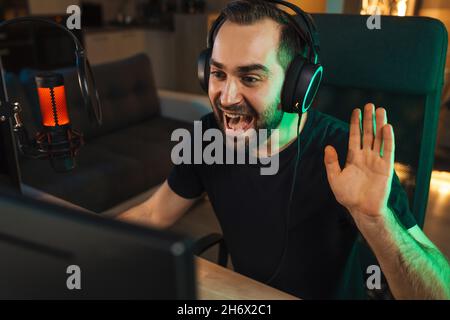 Joyeux jeune homme gmaer streamer dans les écouteurs jouant sur l'ordinateur parler avec les joueurs sur le chat dans la compétition de jeu Banque D'Images