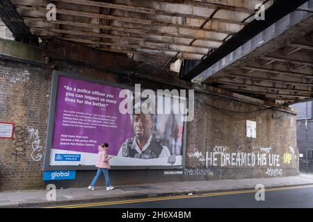 Une femme passe devant un panneau publicitaire pour la Metropolitan police, qui présente un officier de couleur des écoles masculines, sous les ponts ferroviaires de Loughborough Junction, dans le quartier de Lambeth, dans le sud de Londres, le 18 novembre 2021, à Londres, en Angleterre. Banque D'Images