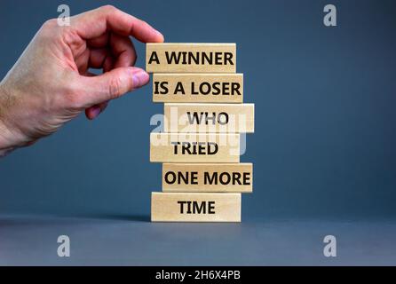 Symbole du gagnant ou du perdant.Blocs de bois avec des mots Un gagnant est un perdant qui a essayé une fois de plus.Magnifique arrière-plan gris, espace de copie.Main d'homme d'affaires. Banque D'Images