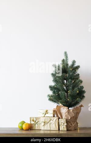 Un petit arbre de Noël avec des ampoules chaudes dans un pot sur une table en bois avec des cadeaux enveloppés dans du papier doré. Le concept de Noël.Photo de haute qualité Banque D'Images